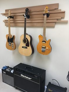 three guitars are hanging on the wall next to an amp