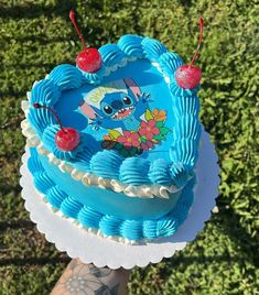 someone holding up a blue cake with cherry toppings on it in front of some grass