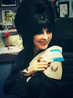 a woman with long black hair and piercings on her arm, smiling at the camera