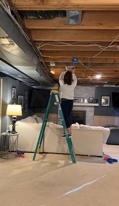 a woman is standing on a ladder and painting the ceiling