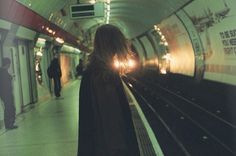 a woman standing in front of a train at a subway station with her back to the camera