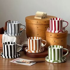 four striped coffee mugs sitting on top of a wooden table next to two boxes