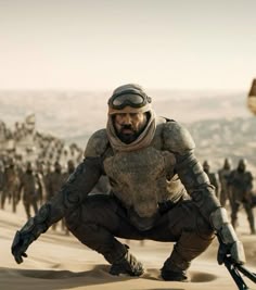 a man kneeling down in the sand with many other people behind him and wearing helmets