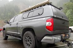the back end of a gray truck parked in a parking lot with mountains in the background