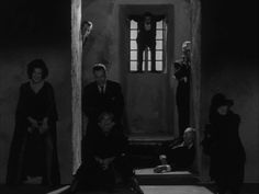 black and white photograph of people standing in front of a door with one person sitting on the floor