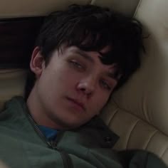 a young man laying in a car seat with his head on the armrests