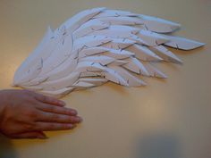 someone is holding out their hand to make a paper angel wings decoration on the wall