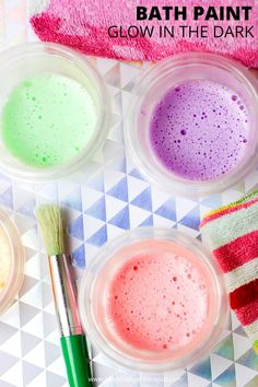 three bowls filled with different colored paint next to two brushes on a checkered tablecloth