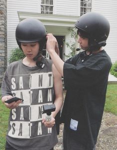 two people wearing helmets standing in front of a house with one person holding a cell phone