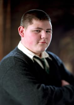 a young man with his arms crossed wearing a sweater and tie