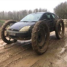a black car driving down a muddy road with large tires on it's wheels