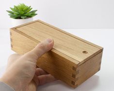 a hand is holding the edge of a wooden box next to a succulent plant