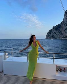 a woman in a long green dress standing on a boat looking at the camera with her arms outstretched