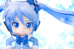 an anime figurine with blue hair wearing headphones and snowflakes in the background