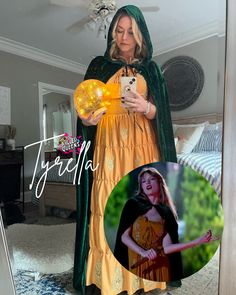 a woman in a yellow dress is looking at her cell phone and wearing a green cape