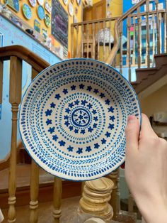 a hand holding a blue and white plate in front of a spiral stair case at a store