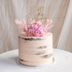 a birthday cake decorated with pink flowers and a happy birthday topper on a white table