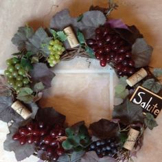 a wreath with grapes, leaves and wine corks is displayed on a table top