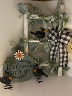 a welcome autumn sign with three birds and a sunflower on the front, sitting next to some fake leaves