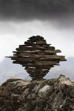 a stack of rocks sitting on top of a rocky hillside under a cloudy sky with dark clouds
