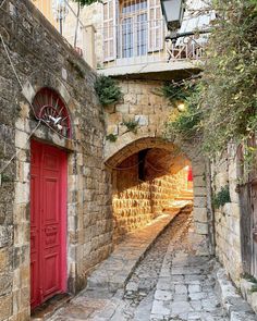 an alleyway with stone walls and red doors leading up to the second story building