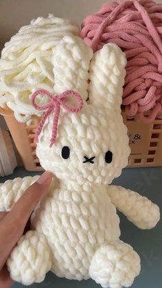 a hand is holding a white crocheted stuffed animal in front of some yarn balls