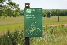 a sign in the middle of a grassy field with trees and grass behind it that says lakeside trail