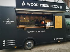 a black food truck parked in front of a building with wood fired pizza on it's side