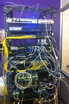 many wires are connected to the back of a server in a room with purple walls