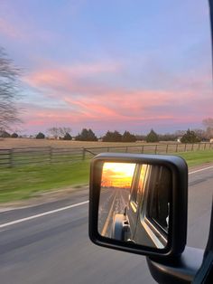 the side mirror of a car as it drives down a highway at sunset or dawn