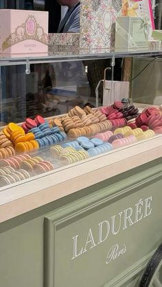 an assortment of colorful macaroons on display in a store window with people looking at them