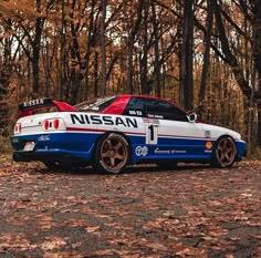 a car that is parked in the dirt next to some trees and leaves on the ground