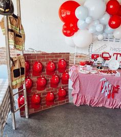 a fireman themed birthday party with red and white balloons on the wall, cake table and ladder