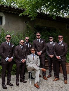a group of men in suits and sunglasses posing for a photo outside with one man sitting on a chair