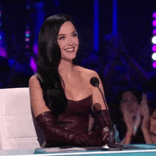 a woman with long black hair is smiling while sitting in front of a microphone