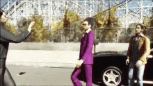 a man in a purple suit is walking down a street with two other men