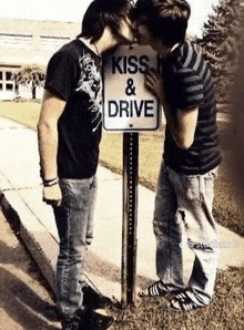 two young men are kissing in front of a sign that says kiss and drive .