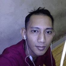 a man wearing a red shirt and earbuds looks at the camera