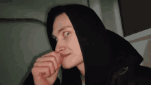 a young man wearing a black hooded jacket looks to the side