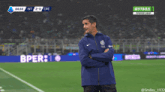 a man in a blue nike jacket stands on a soccer field during a game