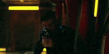 a man in a black jacket is holding a gun in a dark room