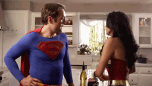 a man dressed as superman stands next to a woman dressed as wonder woman in a kitchen
