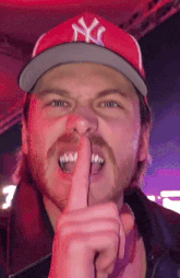 a man wearing a ny yankees hat holds his finger to his lips