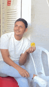a man in a white shirt is sitting in a white chair holding a small yellow object in his hand