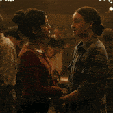 two women are looking at each other in a dark room with christmas lights above them