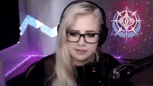 a woman wearing headphones and glasses is sitting in front of a microphone in a room .