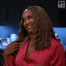 a woman in a pink shirt is smiling and touching her hair ..