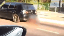 a black car with the hood up is driving down a road .