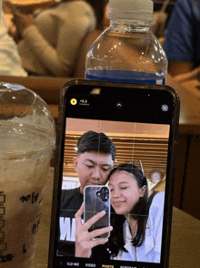 a man and a woman are taking a selfie with a bottle of water behind them