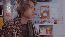 a young man wearing a leopard print jacket is sitting in a room .